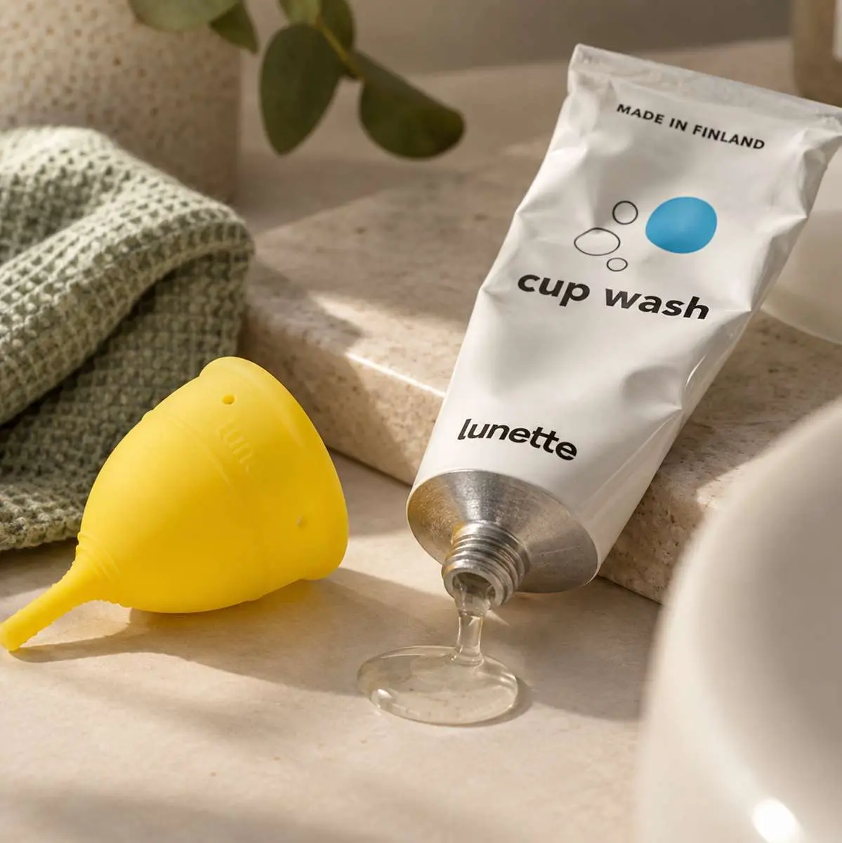 Coupe menstruelle jaune Lunette avec Cup Wash et gel qui coule sur surface minérale dans salle de bains
