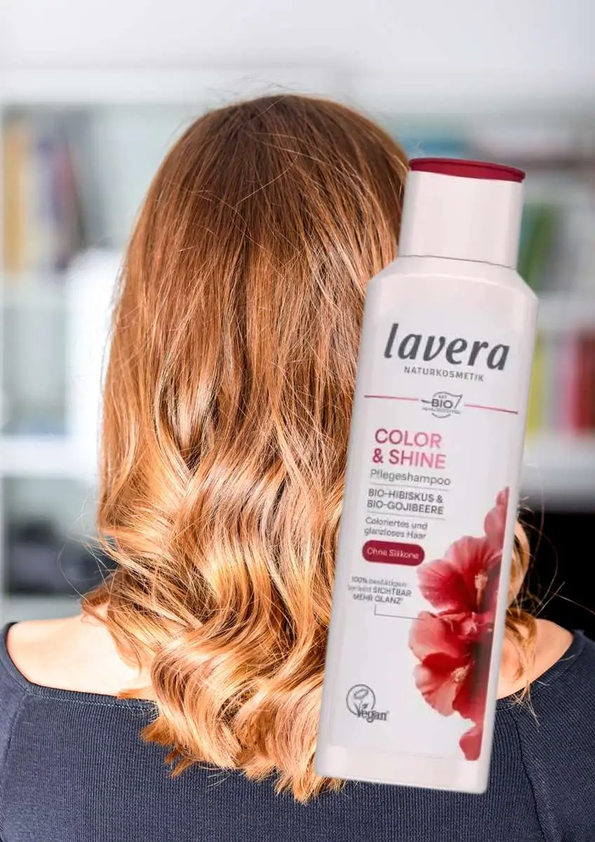 Femme de dos avec cehveux colorés roux brillants et flacon shampoing soin couleur et brillance Lavera
