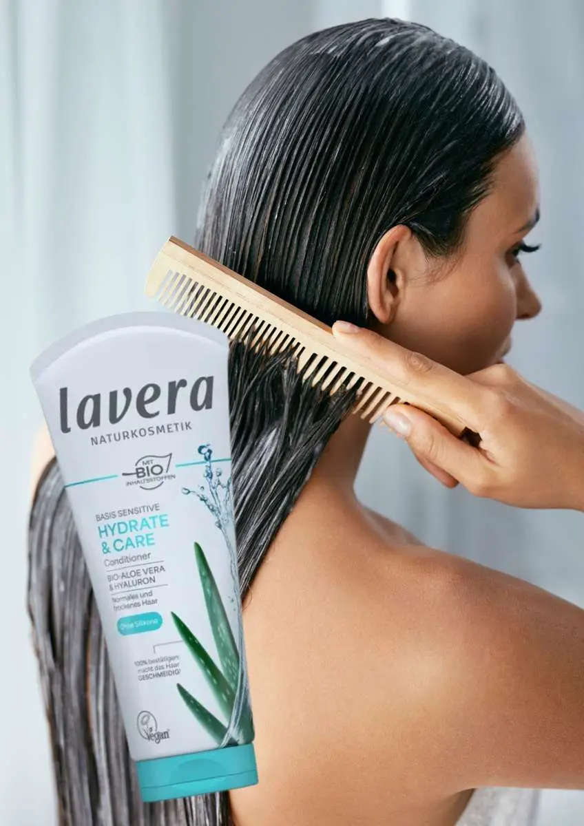 Femme trois-quart dos qui peigne ses cheveux mouillés avec photo shampoing hydratation et soin Basis Sensitive Lavera