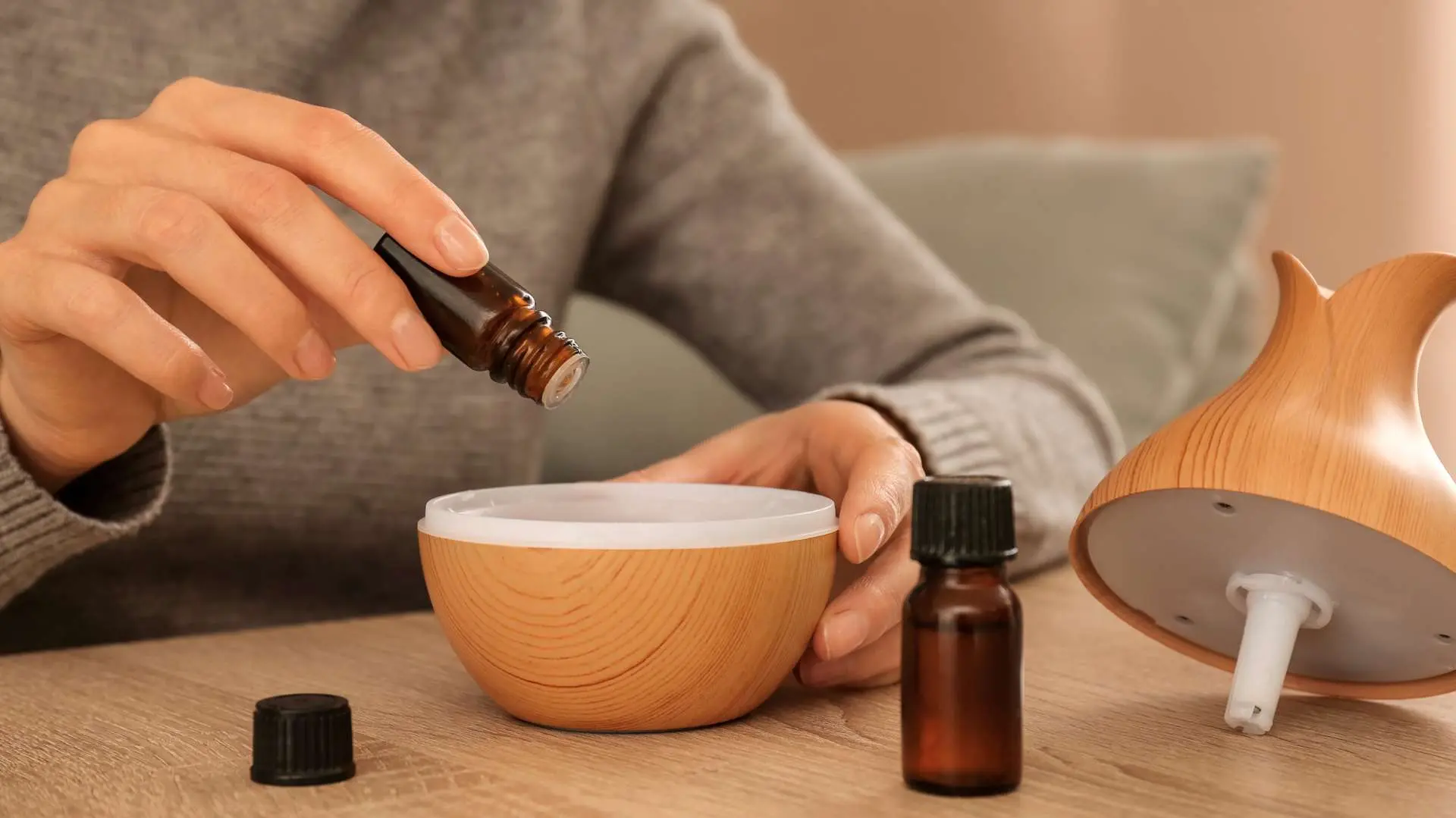 Gros plan mains de femme qui verse de l'huile essentielle dans un diffuseur avec un  autre flacon sur une table en bois