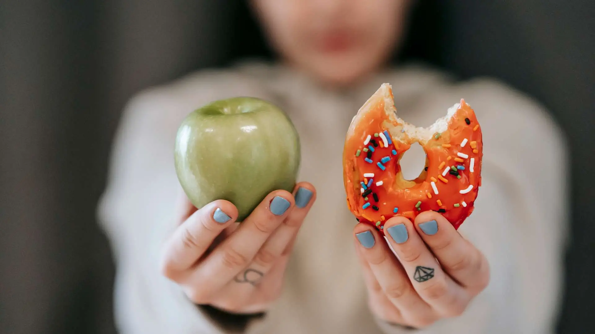 Gros plan femme qui tient une pomme verte dans un main et un donut de l'autre